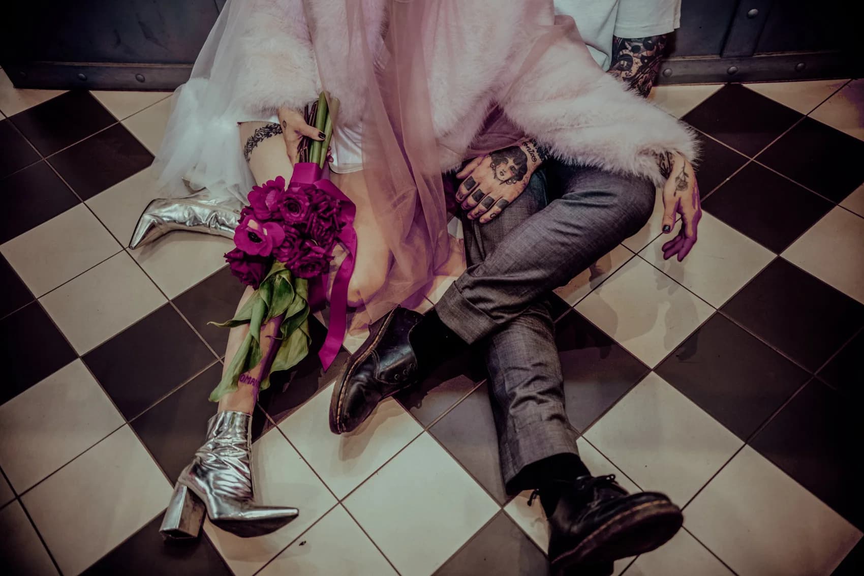 A couple sitting on a chequered floor with a magenta bouquet