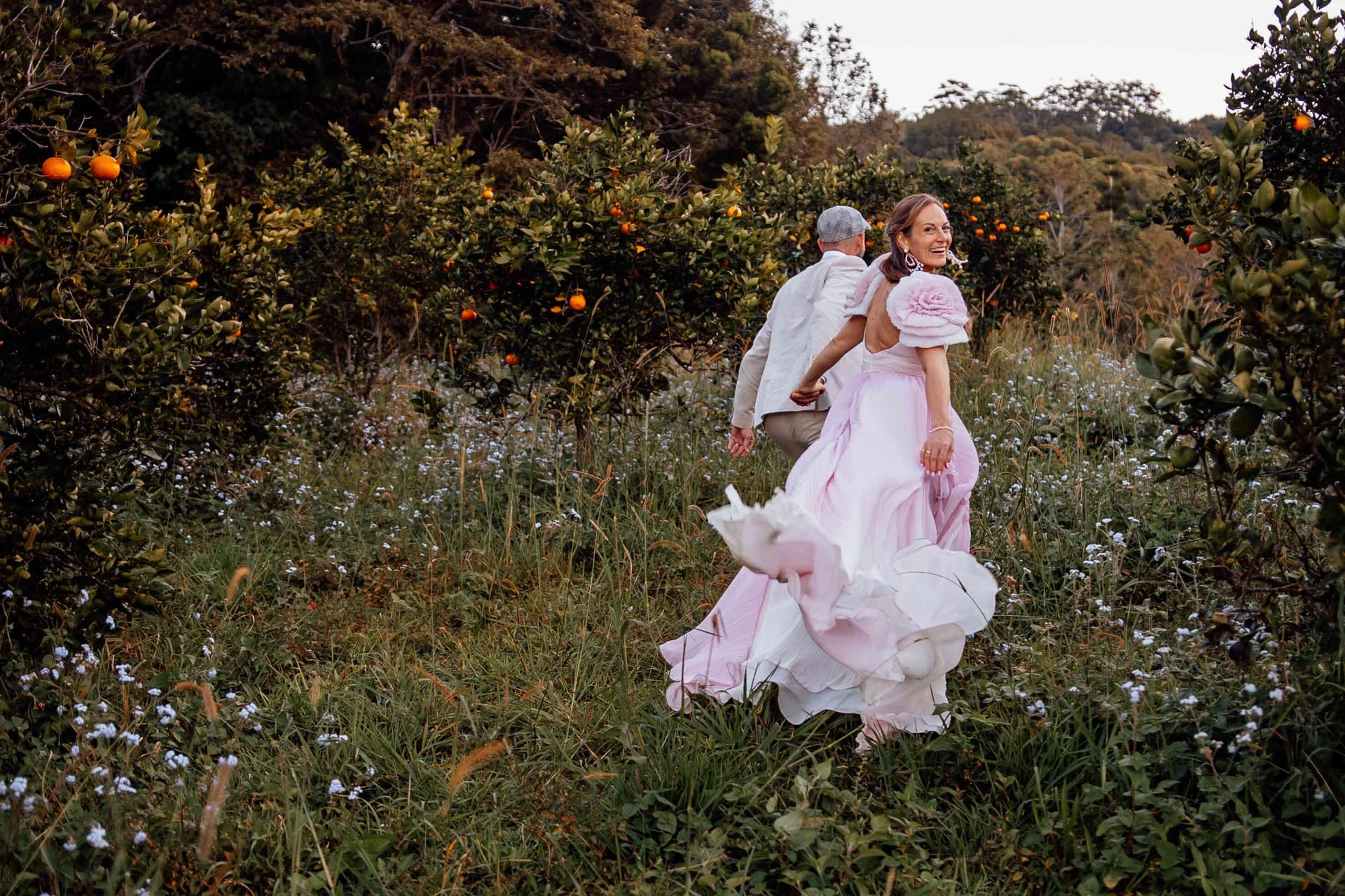 couple_running_through_flower_field_orchard_pink_dress_1e347e7799